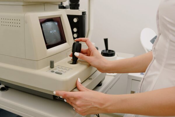 Side view of crop faceless female ophthalmologist using autorefraktometer for corneal topography in contemporary medical office