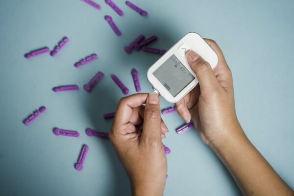 Top view of crop anonymous female diabetic measuring blood sugar with glucometer over scattered lancets